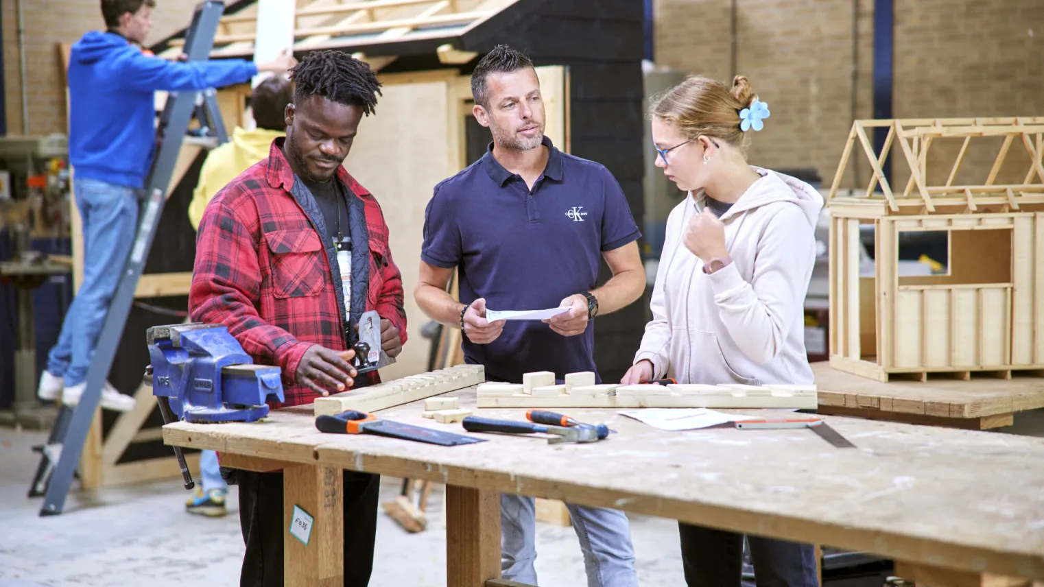 Studenten van de opleiding meubelmaker werken samen in de werkplaats met een docent 