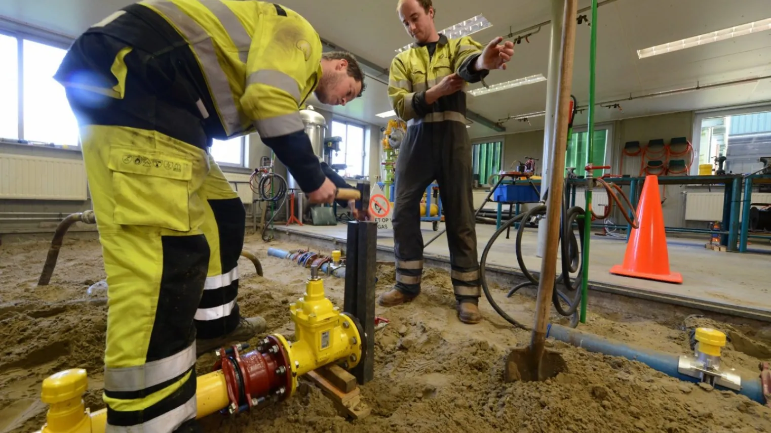 Twee monteurs gas-, water- en warmtedistributie werken aan een leiding op een bouwplaats. 