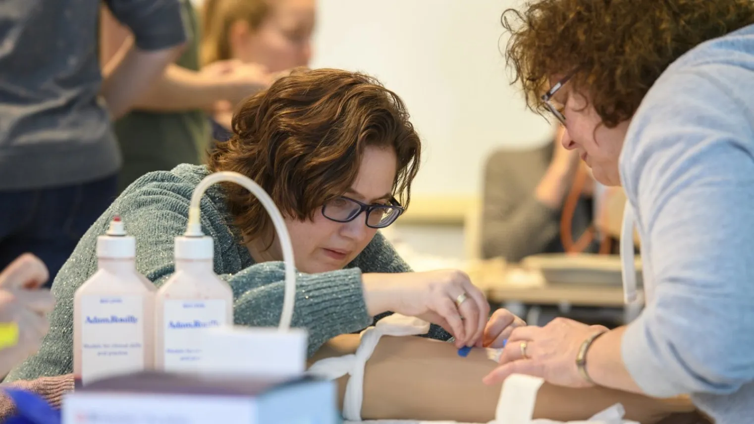 Verpleegkundige oefent met inbrengen infuus tijdens examentraining Verpleegkundige vaardigheden bij andere deelnemer. 