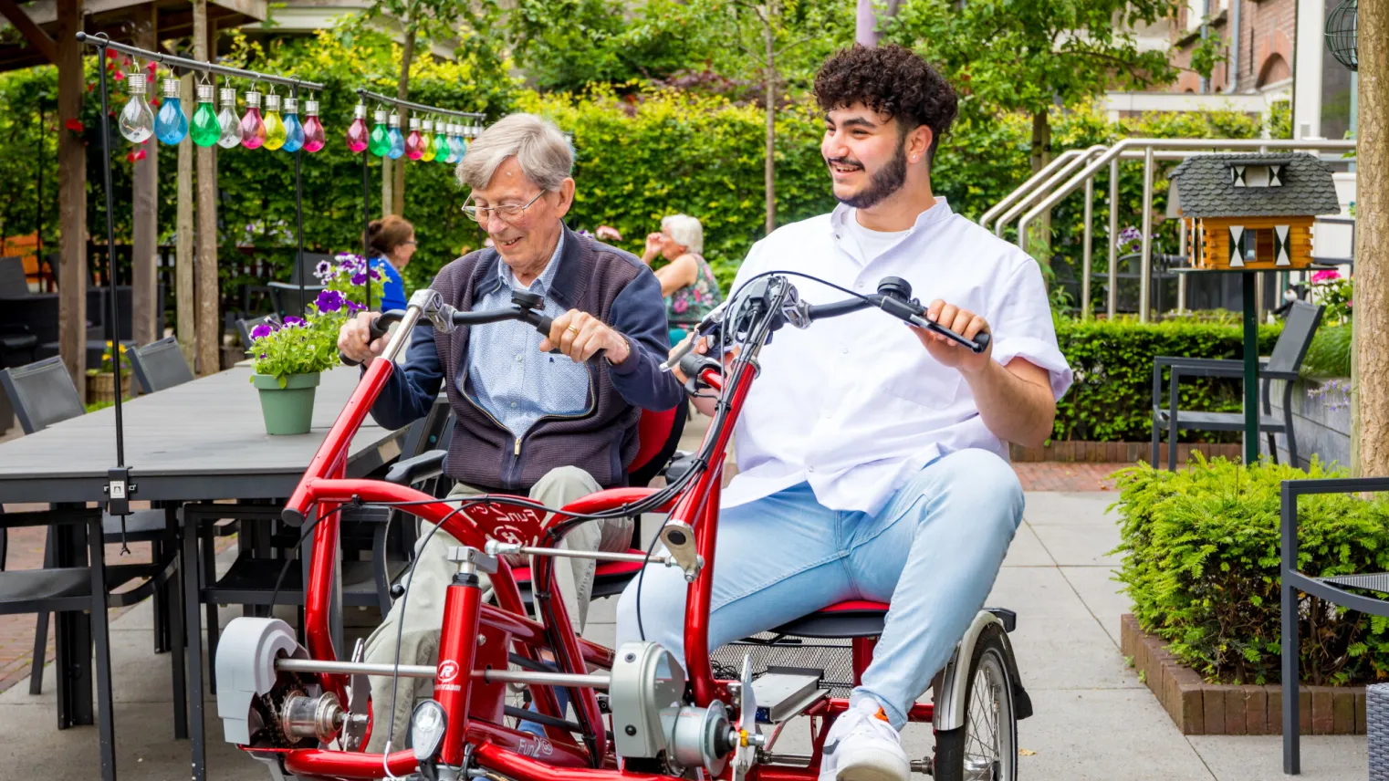 Man en verzorger zitten samen op een fiets voor twee personen. 