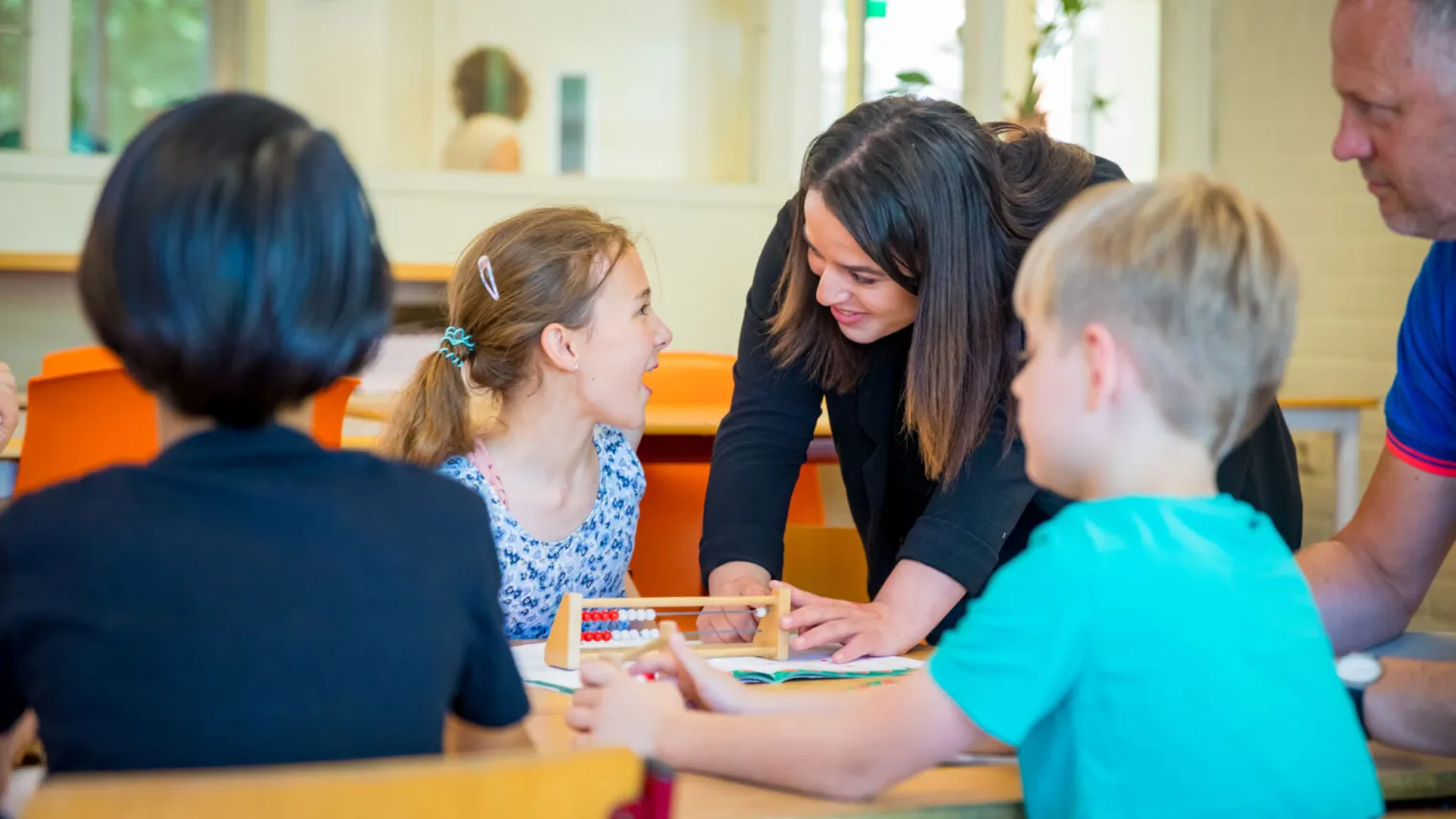 Klaslokaal met leraar en kinderen aan tafel. 