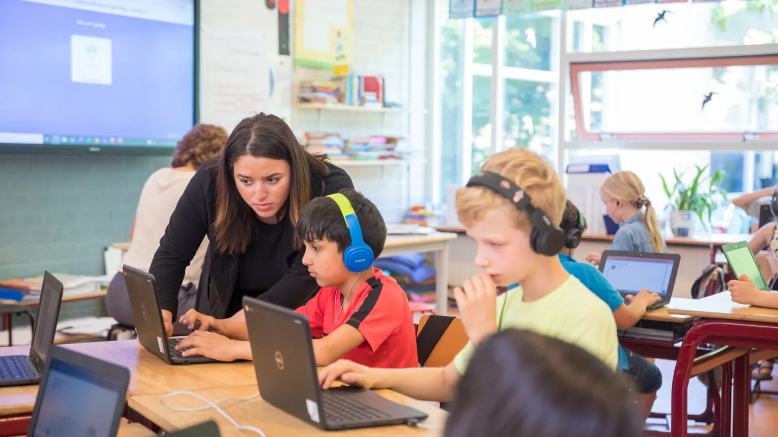 Klaslokaal met kinderen en laptops, leraar geeft les