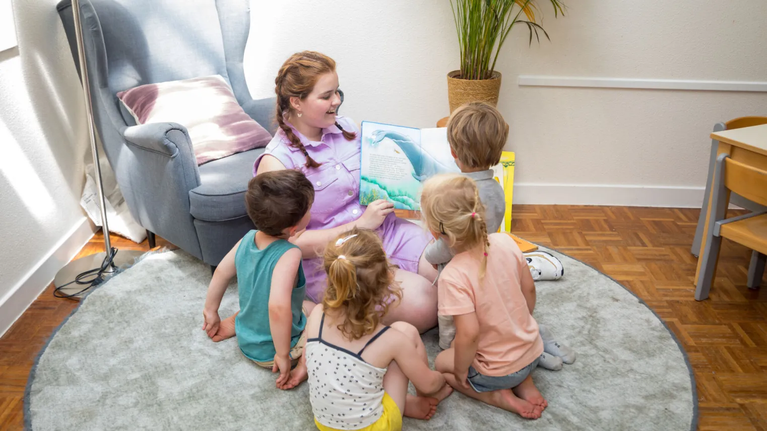 Een vrouw zit op een kleed met kinderen eromheen. 