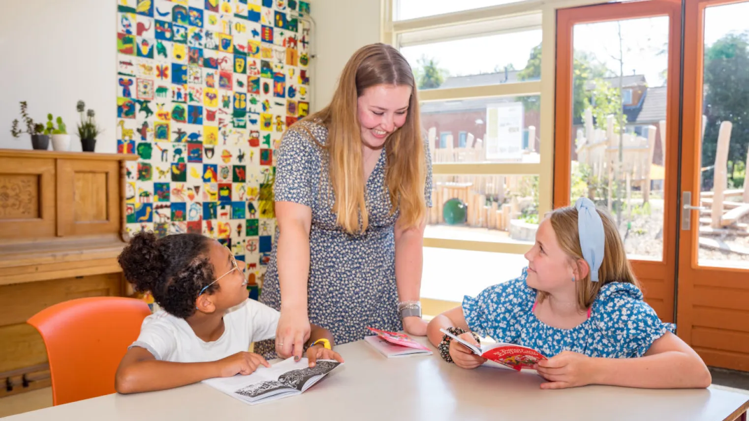 Een jonge vrouw en twee kinderen zitten aan tafel met boeken.