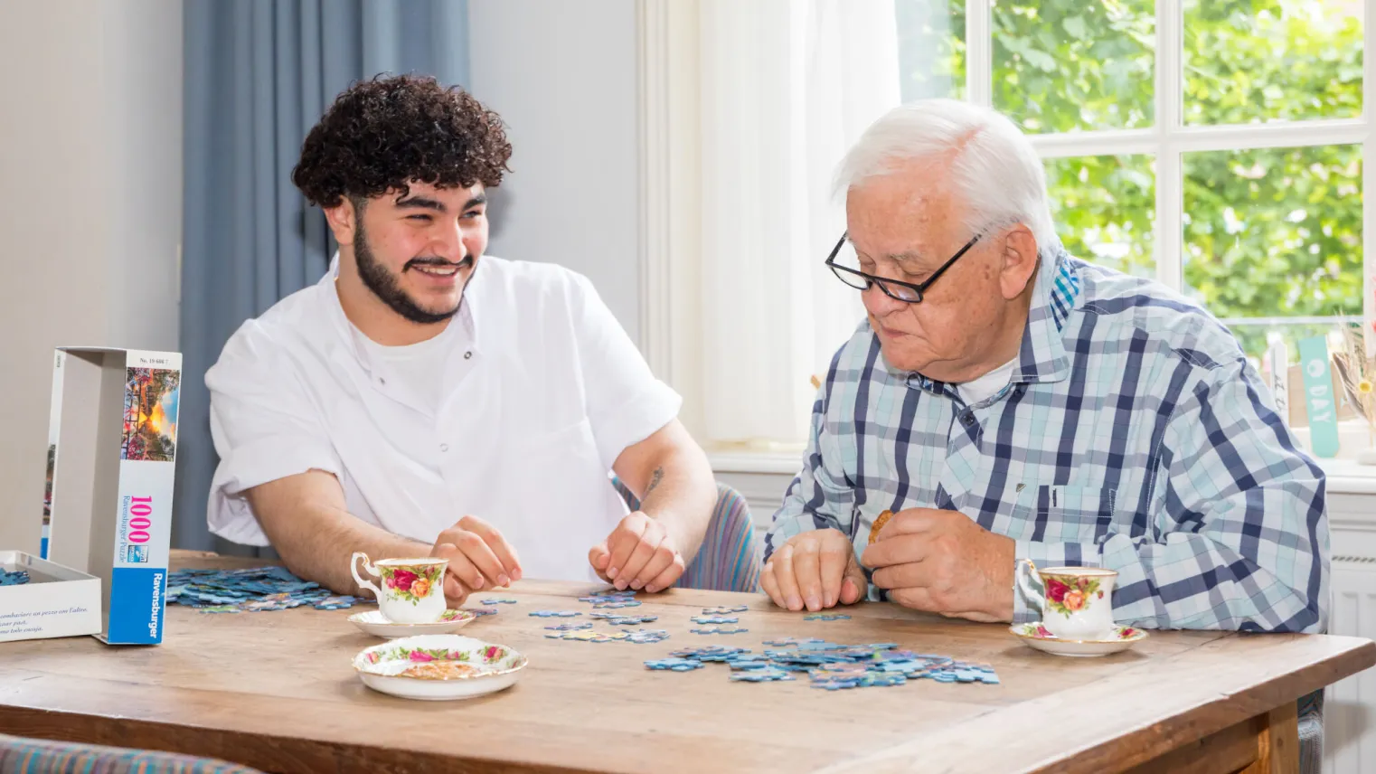 Een jonge man en een oudere man maken samen een legpuzzel. 