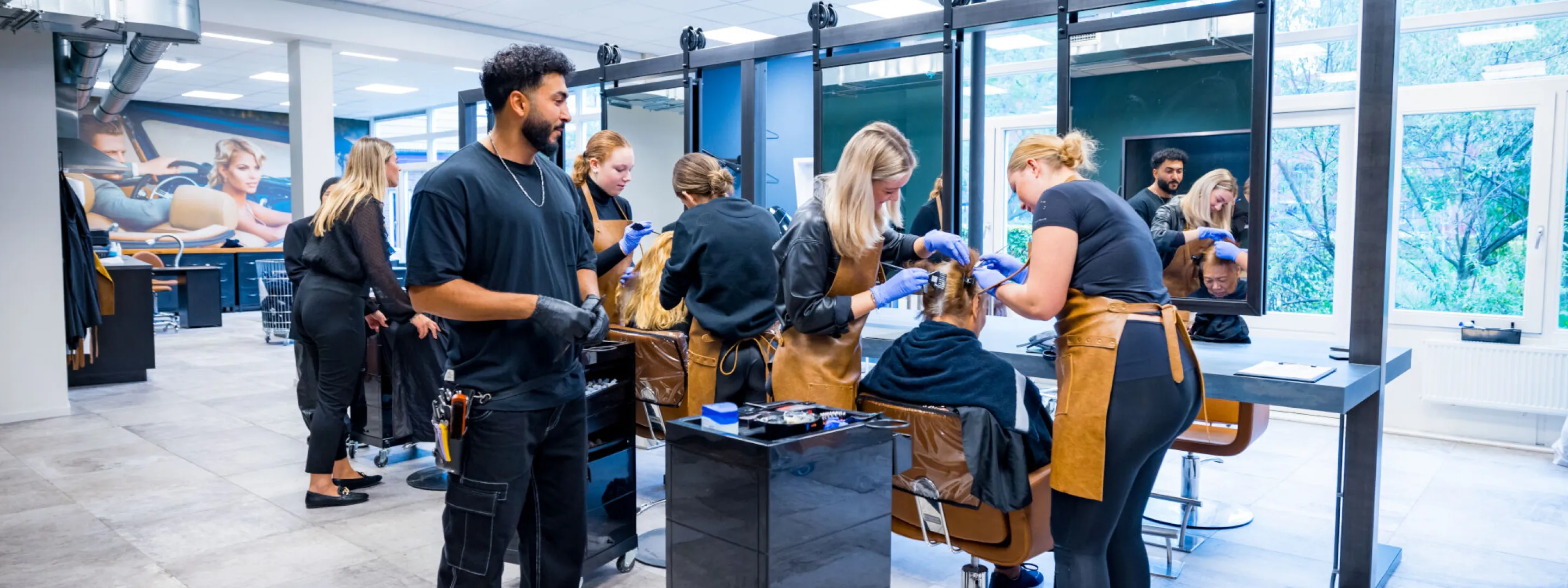 Meerdere kappers in opleiding bezig met kleuren van haren bij proefklanten in een kapperslokaal